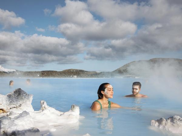 A woman and man with white face masks soak in a steaming, milky blue thermal lagoon.