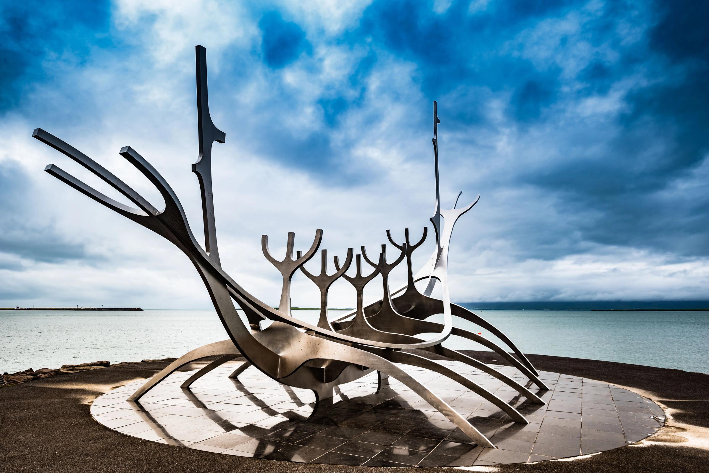 a sculpture of a boat is sitting on the shore of a lake .