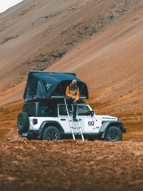 a man is sitting on top of a jeep with a tent on top of it .