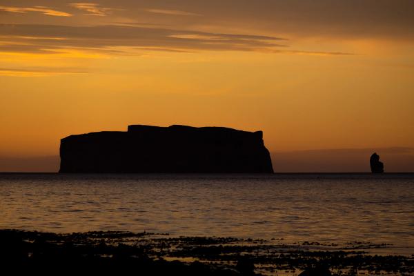 Silhouettes of a flat-topped island and a sea stack against an orange sunset.