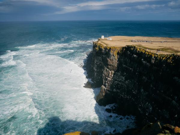 a cliff with cars and a lighthouse on top over a wild sea
