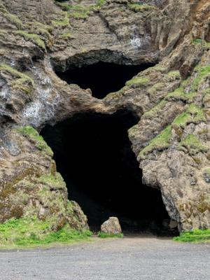 Two dark cave entrances in a rugged, moss-covered rock face above a gravel path.