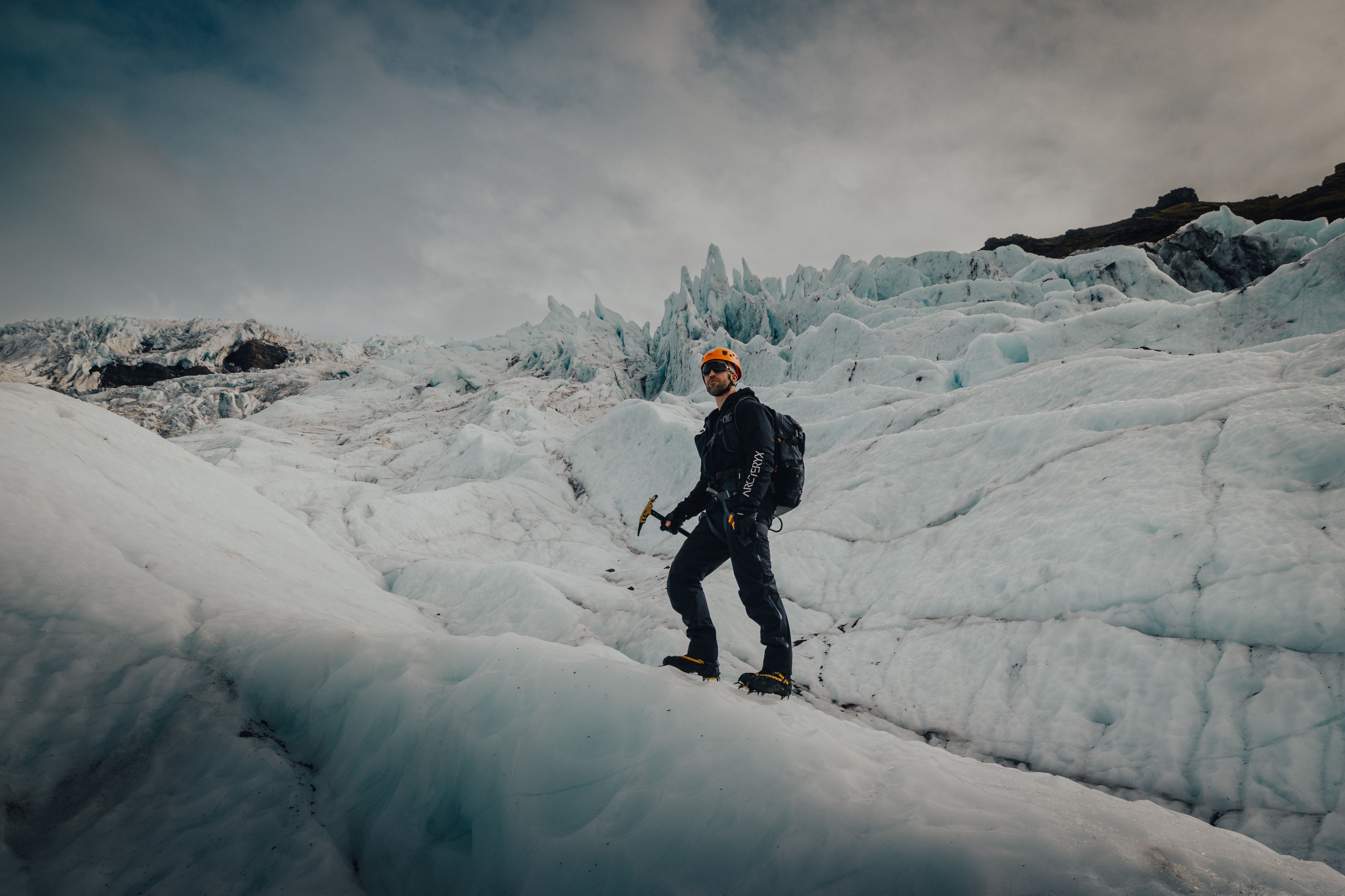 A person with a helmet, ice axe, and backpack stands on a glacier.