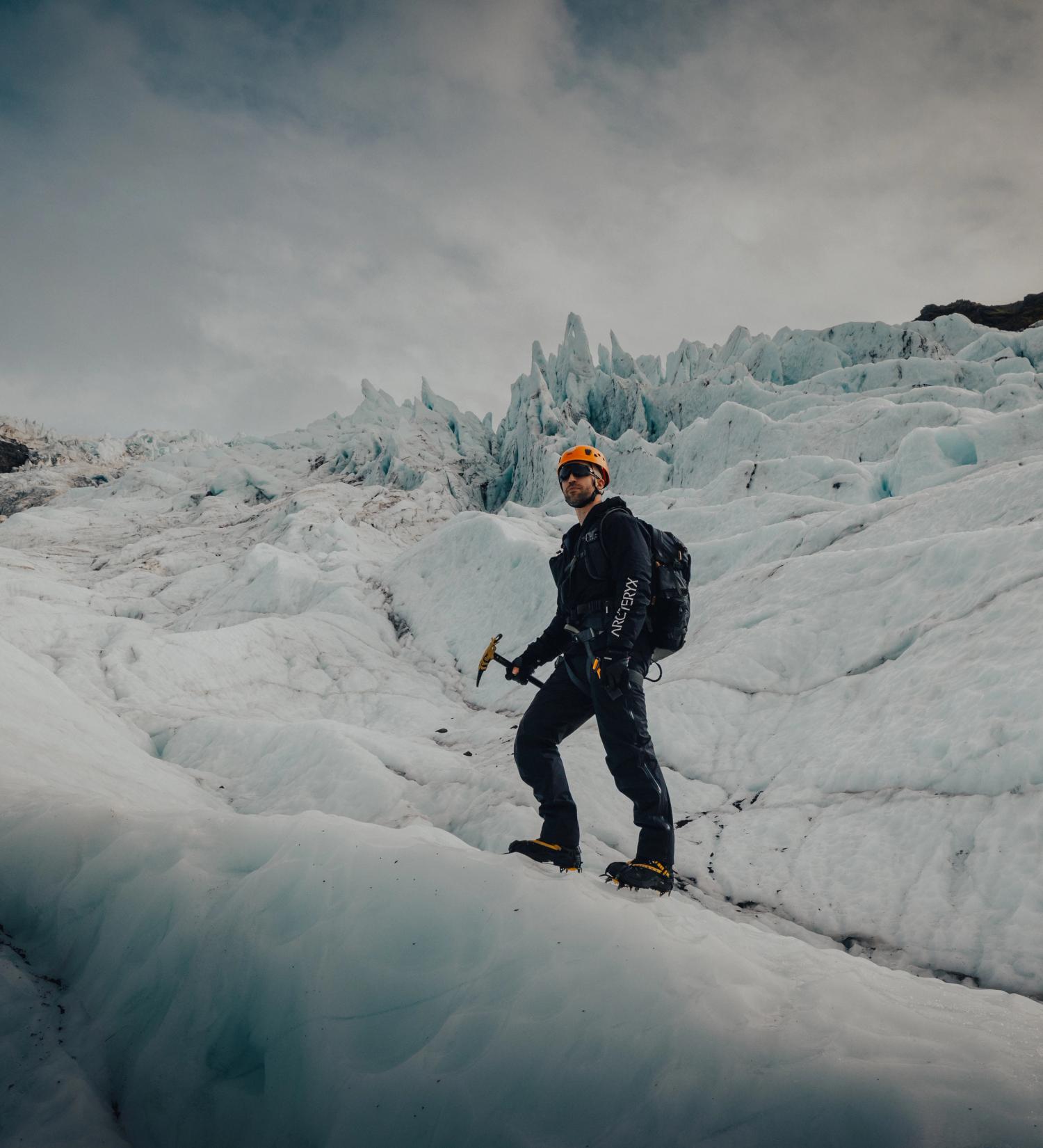 A person with a helmet, ice axe, and backpack stands on a glacier.