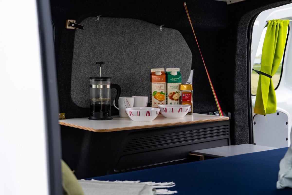 Primer plano de la mesa con cafetera de émbolo, tazas, cuencos y envases de zumo preparados para el desayuno
