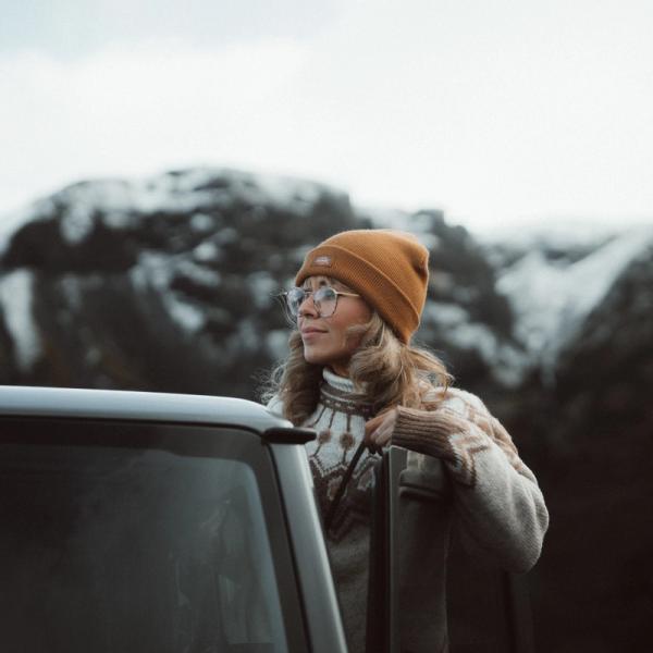 Girl with an orange hat and glasses outside her car gazing at the horizon