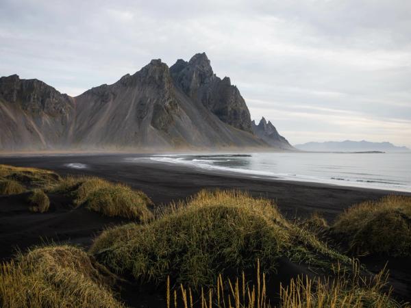 there is a black sandy beach with mountains in the background .