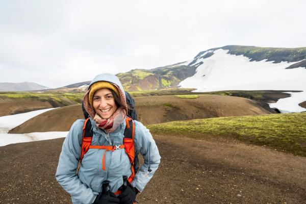 Smiling hiker in a beanie and jacket against a background of snowy, mossy hills.