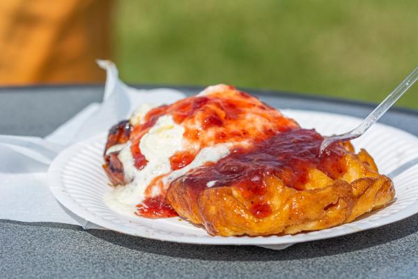 Fried dough topped with melting ice cream and strawberry jam, on a paper plate with a fork.