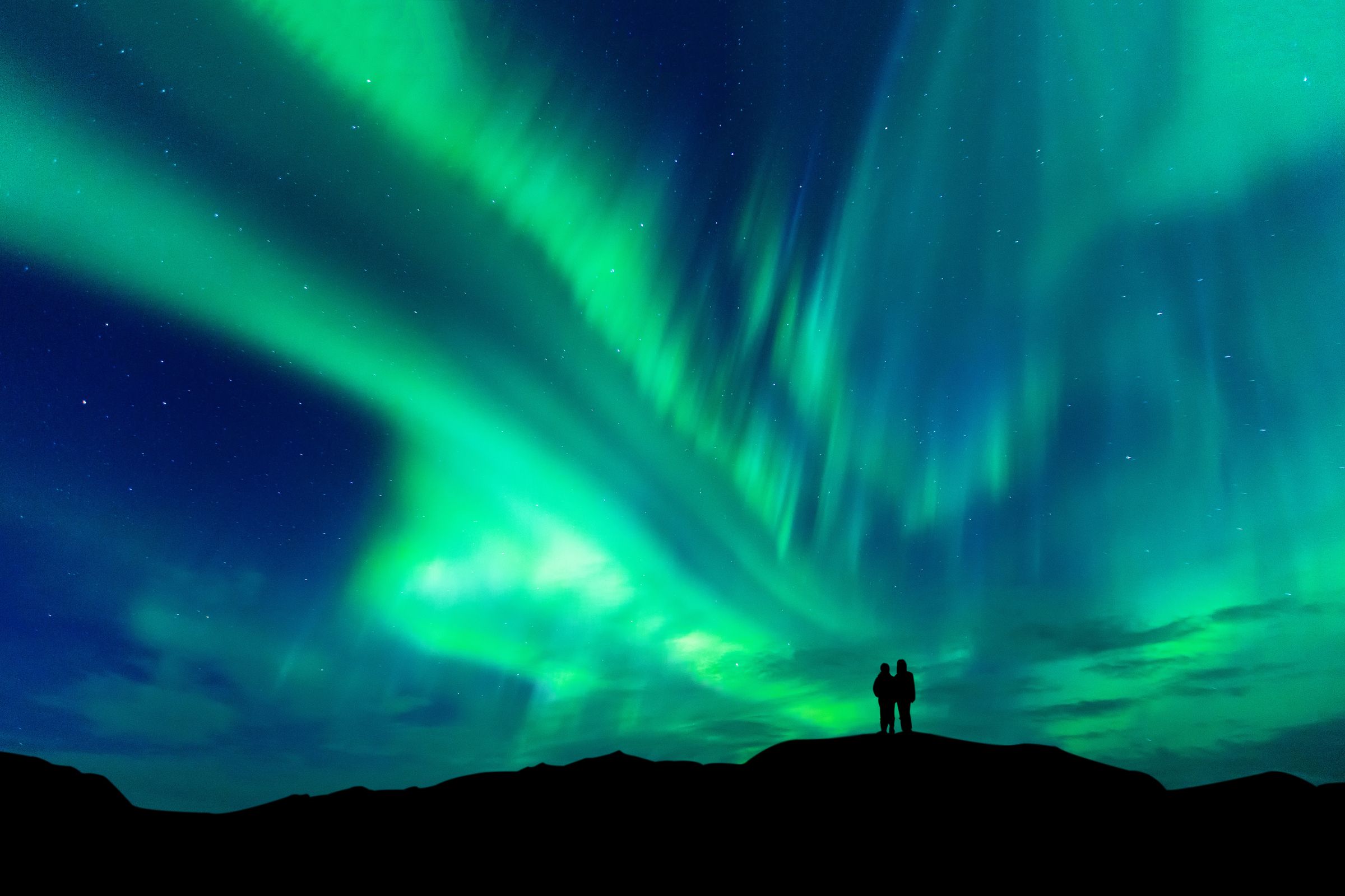 two people are standing on top of a hill watching the aurora borealis .