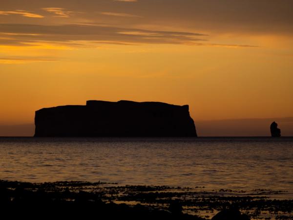 Silhouetted sea cliffs and a sea stack against a vibrant orange sunset sky.