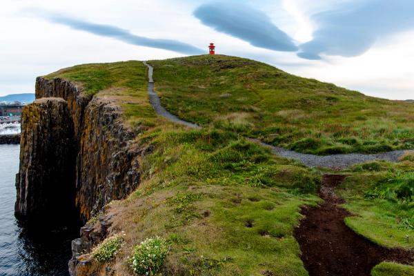 un pequeño faro de color naranja en la cima de una verde colina