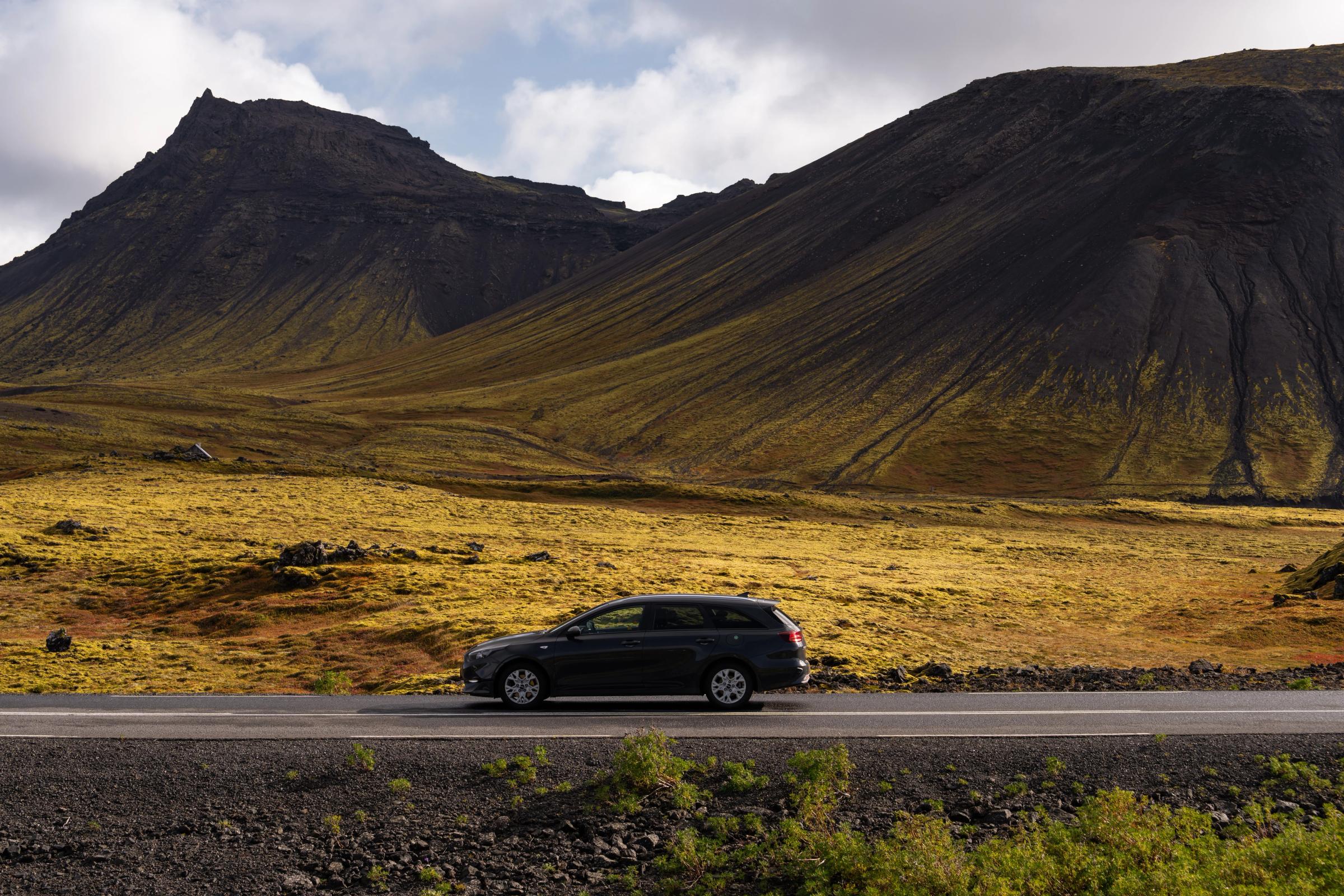 Kia Ceed familiar circulando por una carretera asfaltada en un paisaje montañoso abierto, alquiler de coches en Islandia