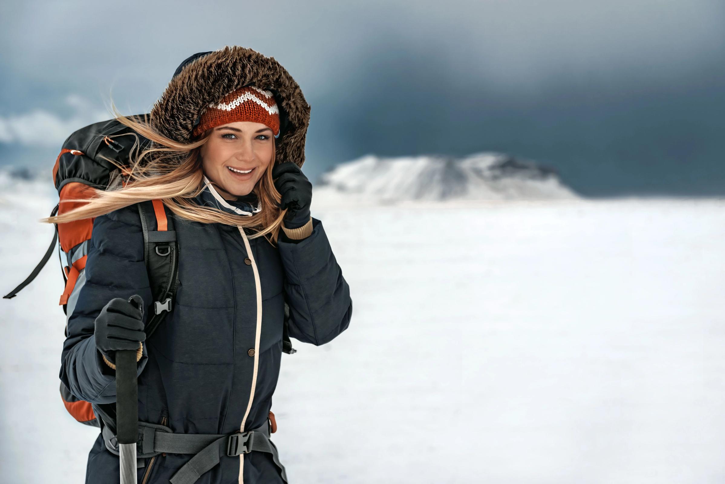 a woman with a backpack and hiking poles is standing in the snow .