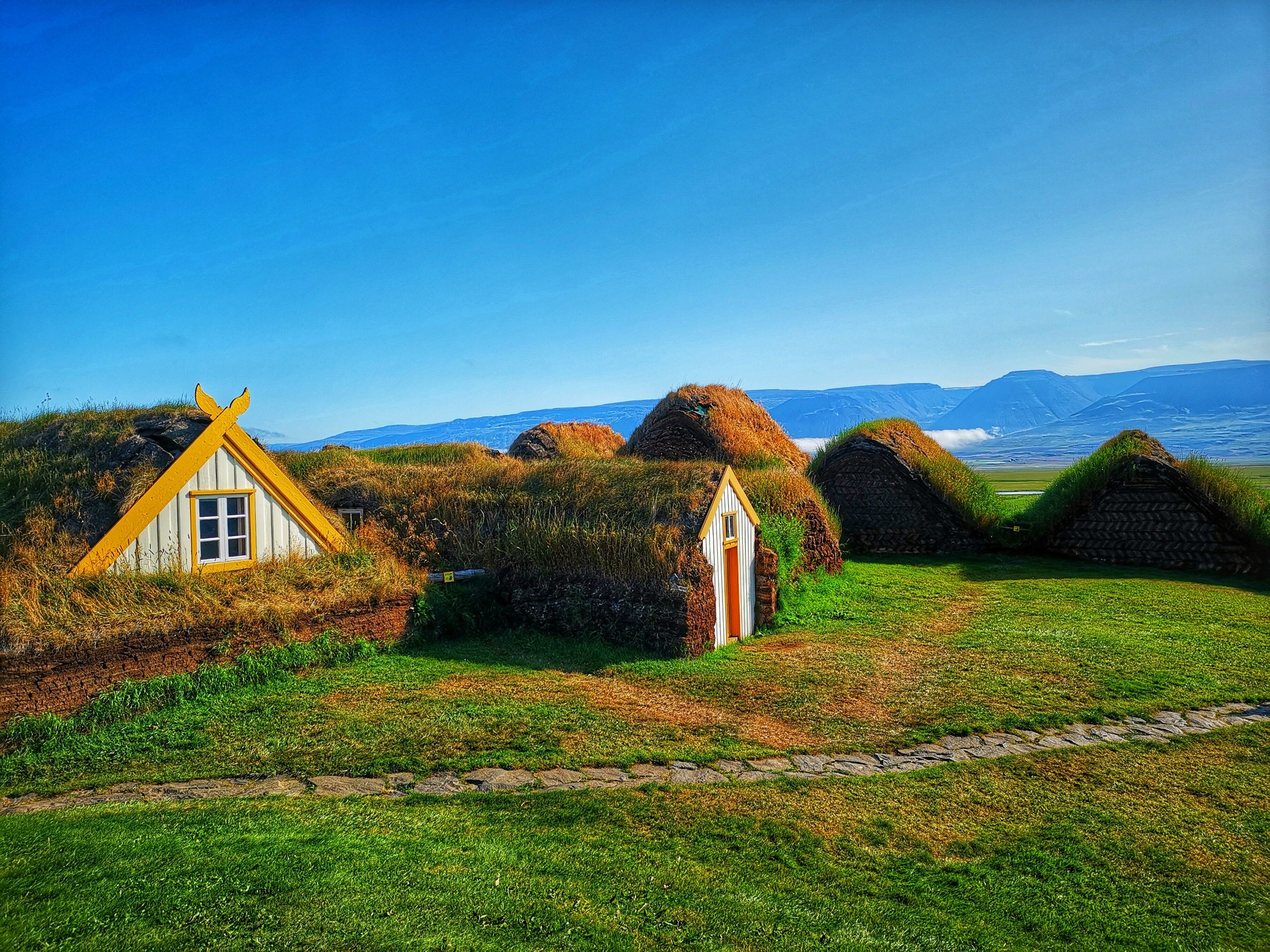 a group of grass covered houses in a field with mountains in the background at Glaumbær in Iceland.