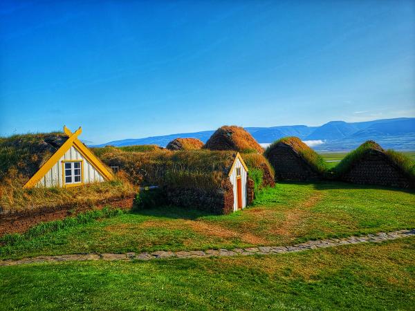 a group of grass covered houses in a field with mountains in the background at Glaumbær in Iceland.