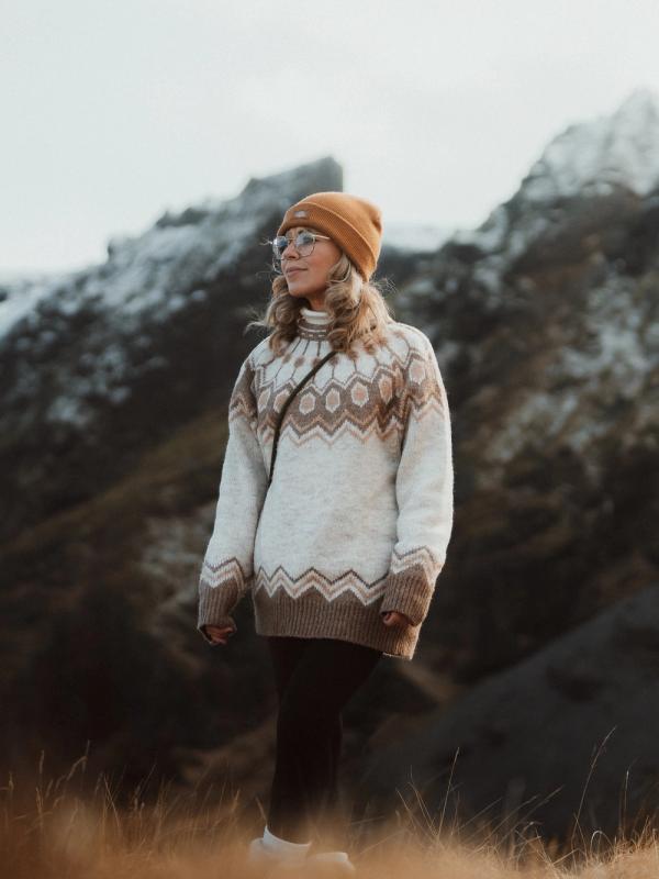 a woman in a sweater and hat is standing in a field in front of a mountain .