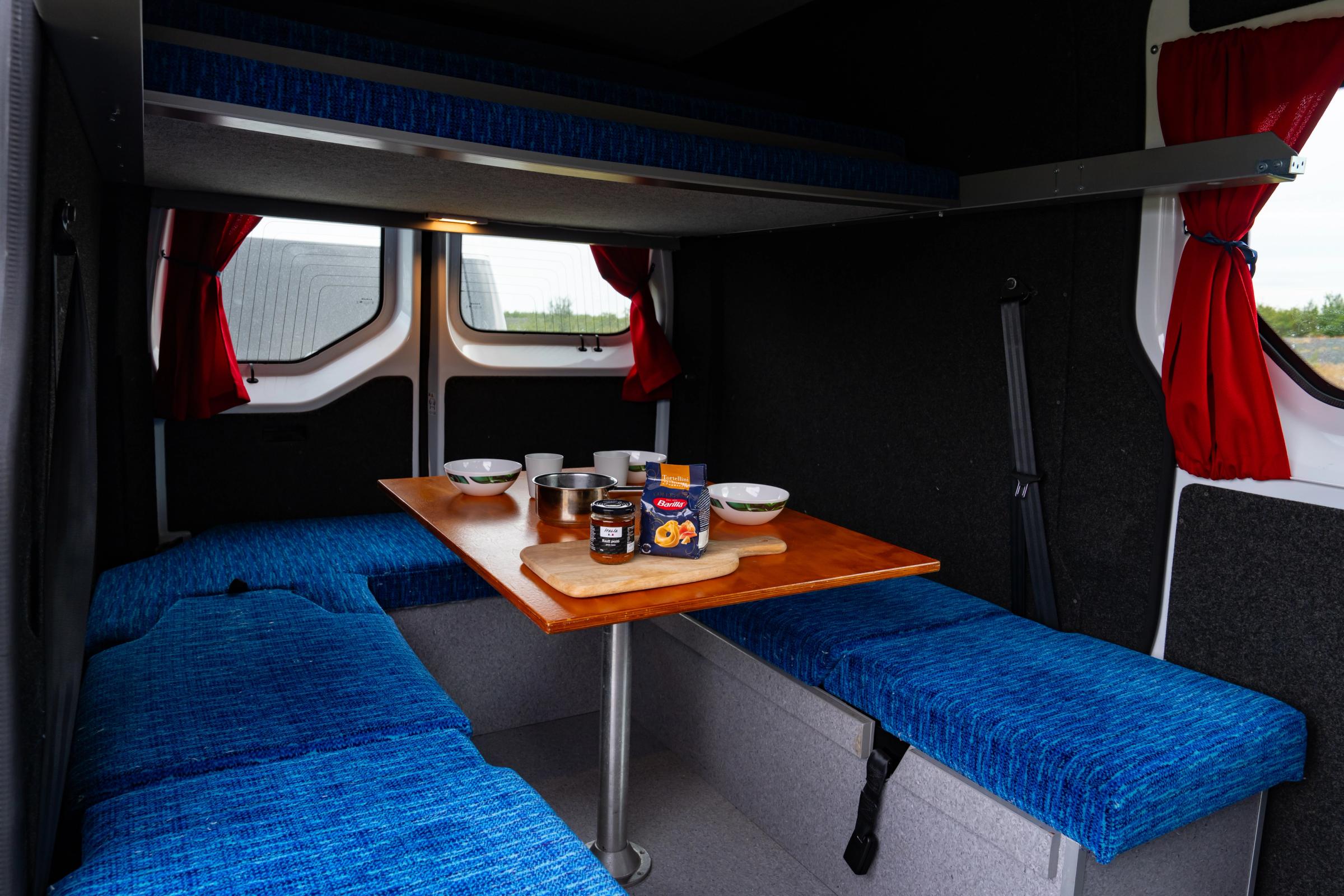 Rear bench seating around a table set with bowls, cups and a cutting board, upper bed above