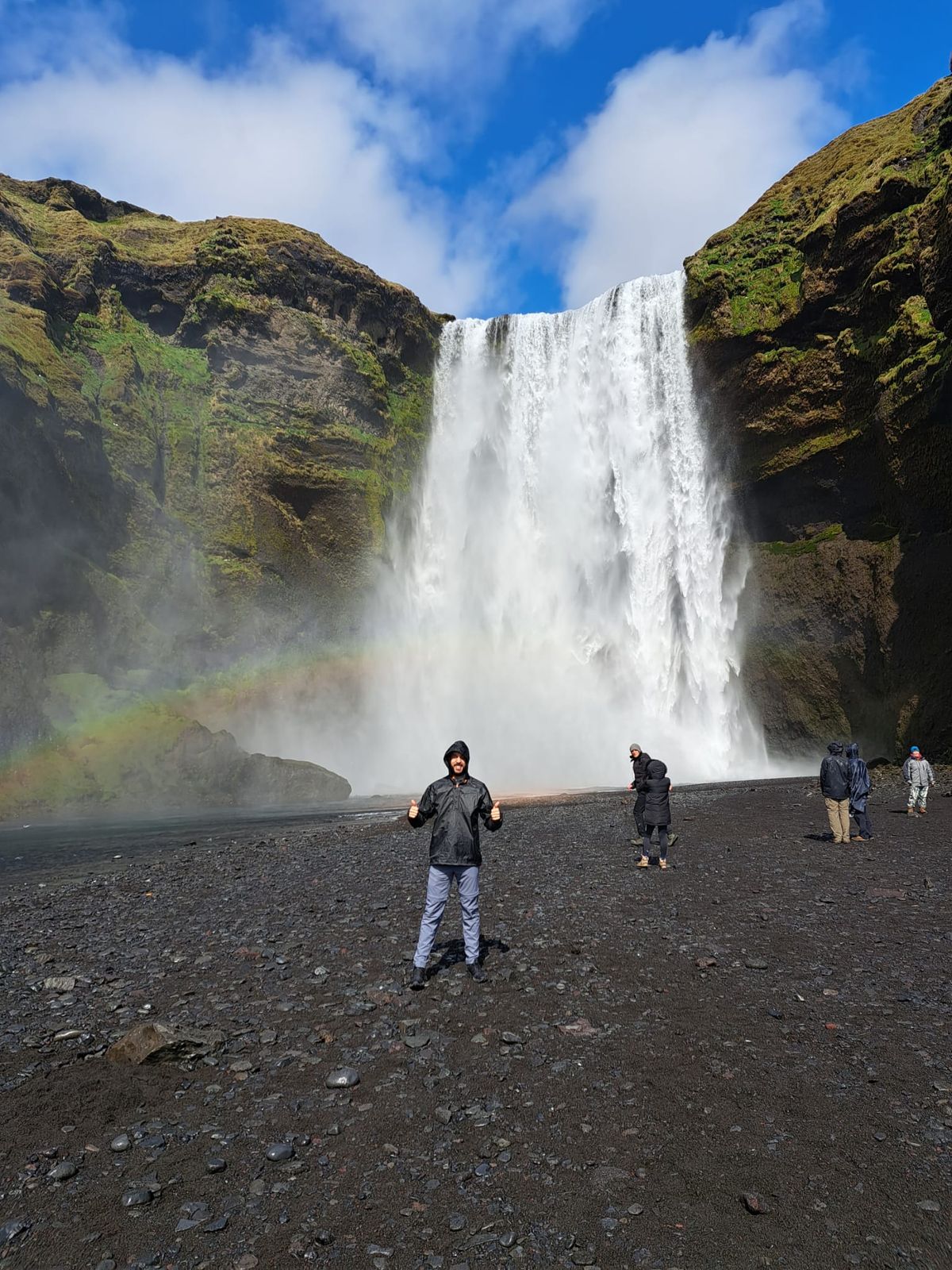 un hombre está de pie frente a una cascada con un arcoíris de fondo