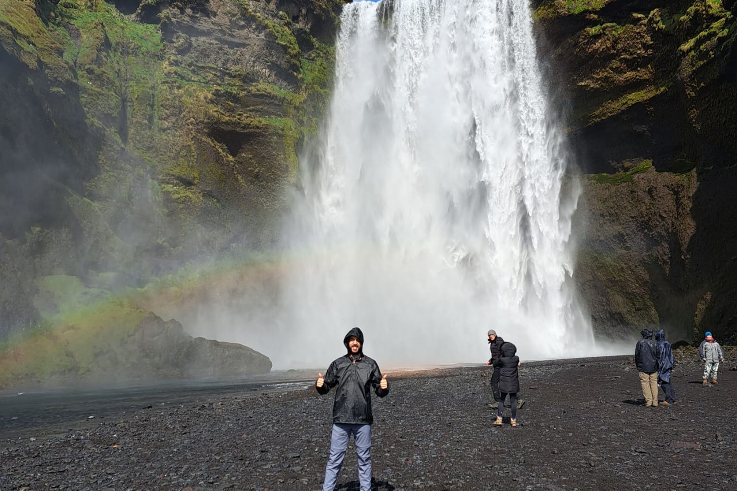 un hombre está de pie frente a una cascada con un arcoíris de fondo