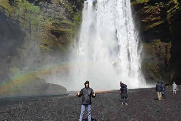 un hombre está de pie frente a una cascada con un arcoíris de fondo