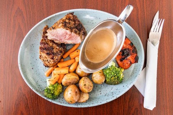 a plate of food with meat , vegetables and gravy on a wooden table .