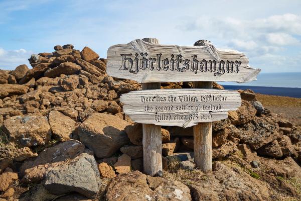 A wooden sign on a rocky mound reads "Hjörleifshaugar," marking the spot where Viking Hjörleifur, Iceland's second settler, was killed circa 875 A.D.