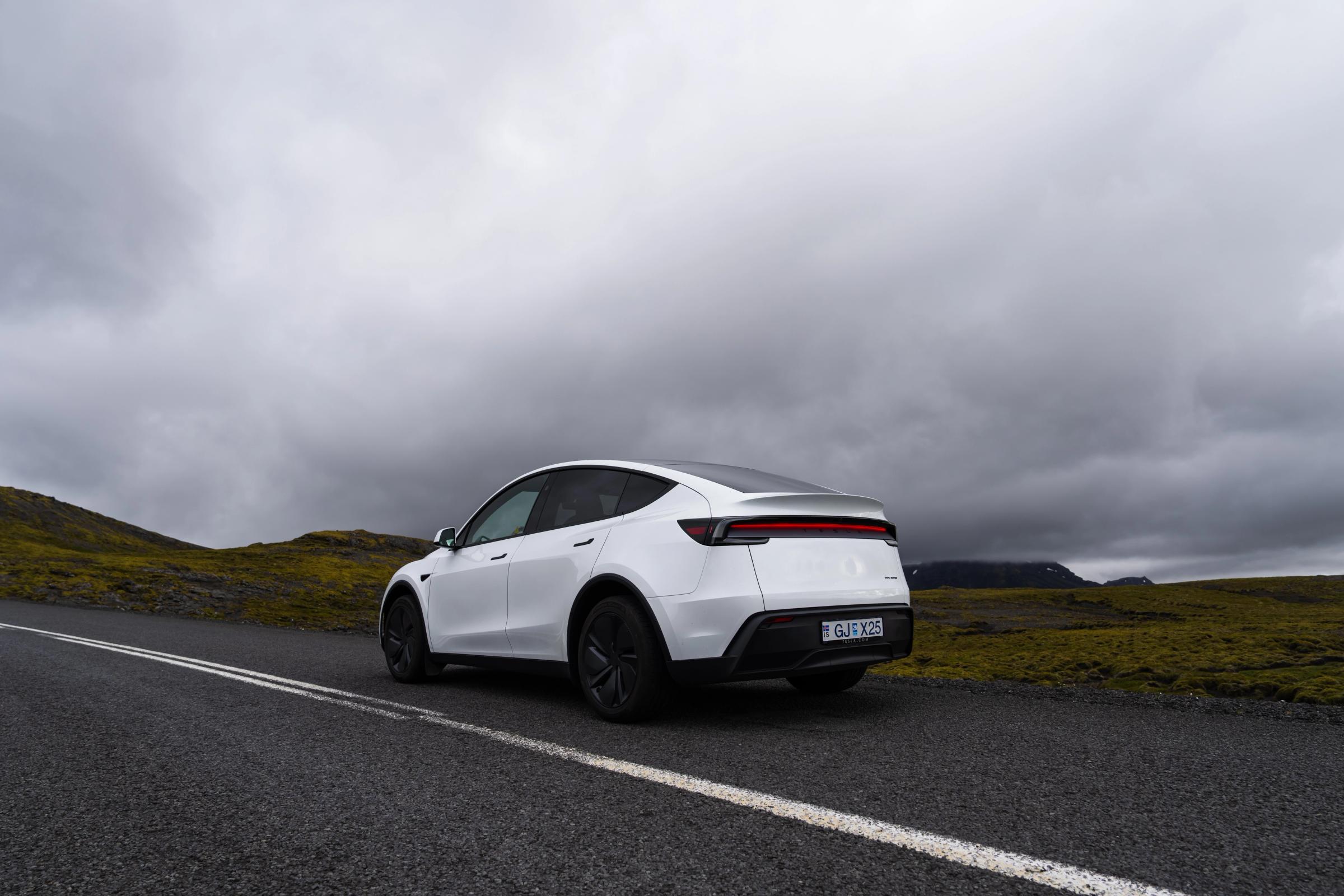 Vista trasera de un Tesla Model Y en una carretera islandesa, coche eléctrico de alquiler con colinas cubiertas de musgo en los alrededores