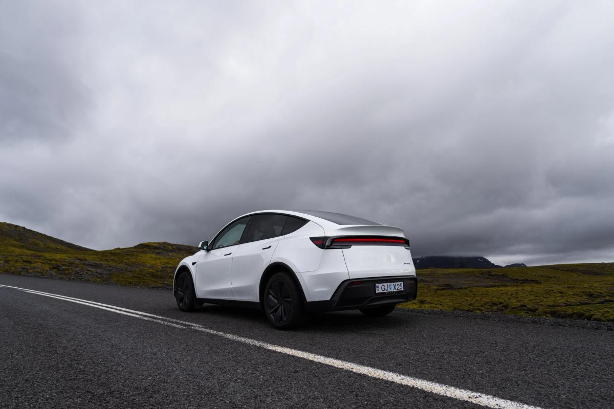 Vista trasera de un Tesla Model Y en una carretera islandesa, coche eléctrico de alquiler con colinas cubiertas de musgo en los alrededores