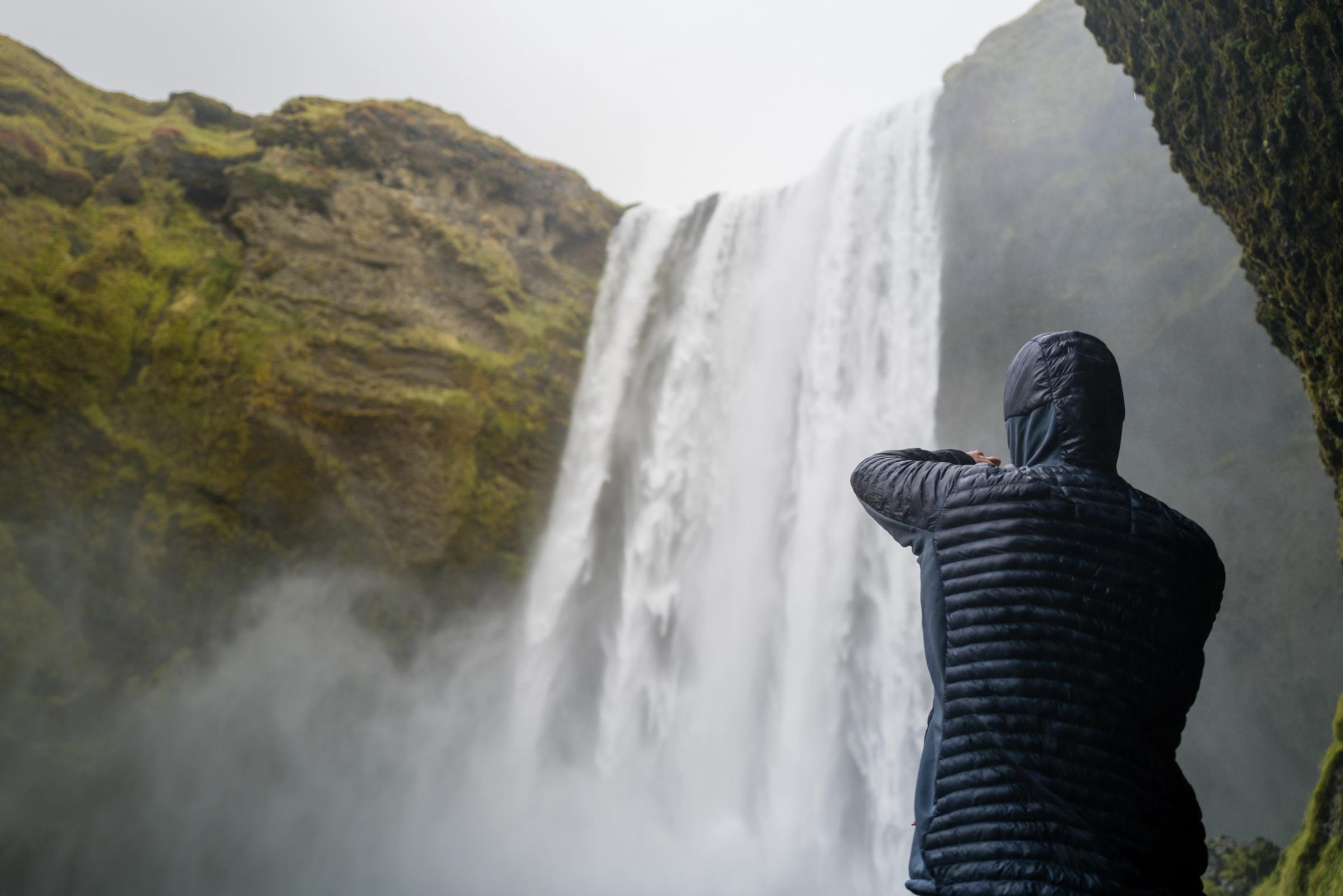una persona con una chaqueta con capucha está parada frente a una cascada.