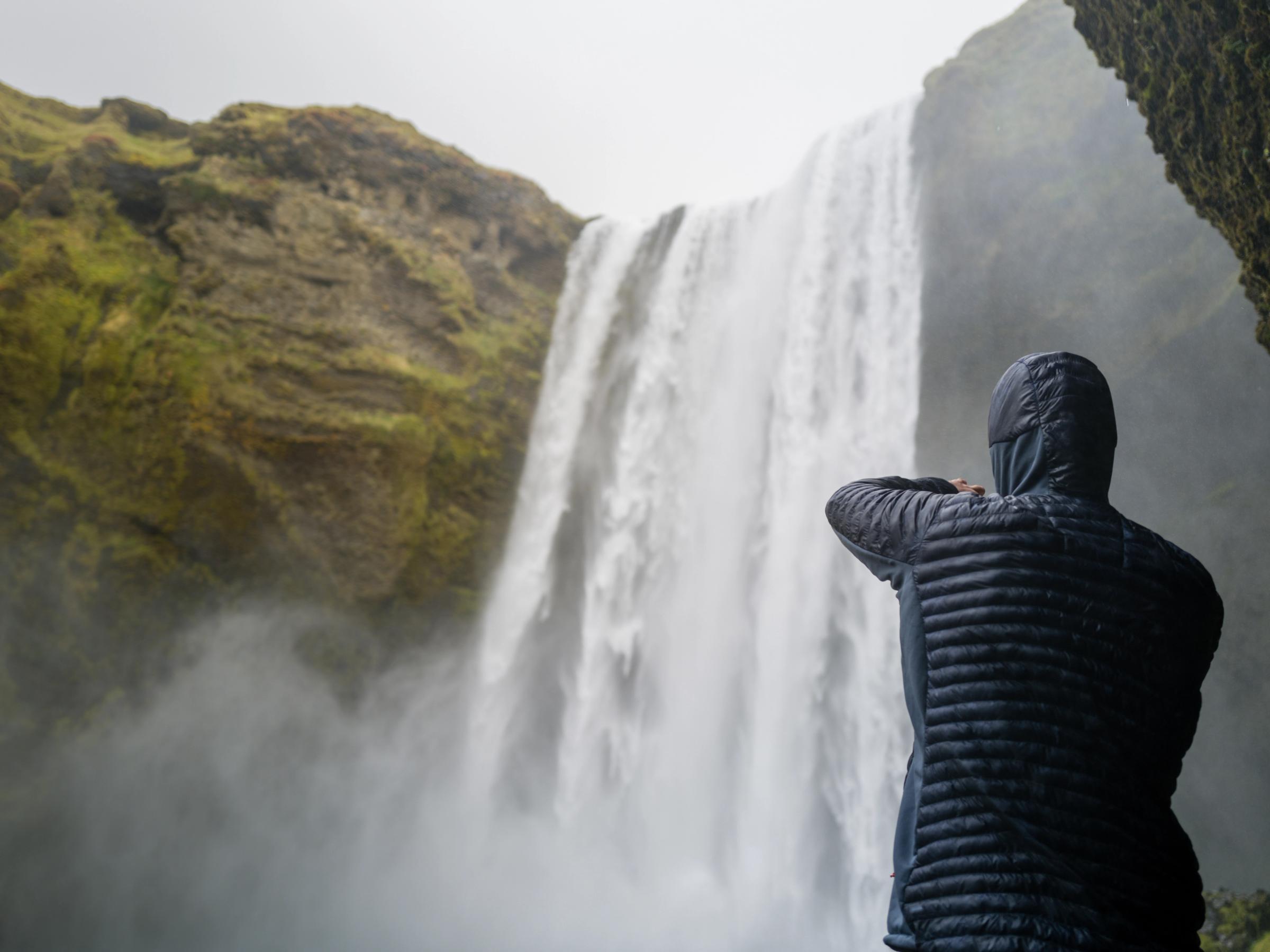 una persona con una chaqueta con capucha está parada frente a una cascada.