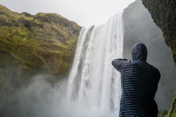 a person in a hooded jacket is standing in front of a waterfall .