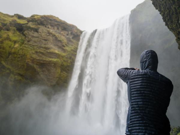 una persona con una chaqueta con capucha está parada frente a una cascada.