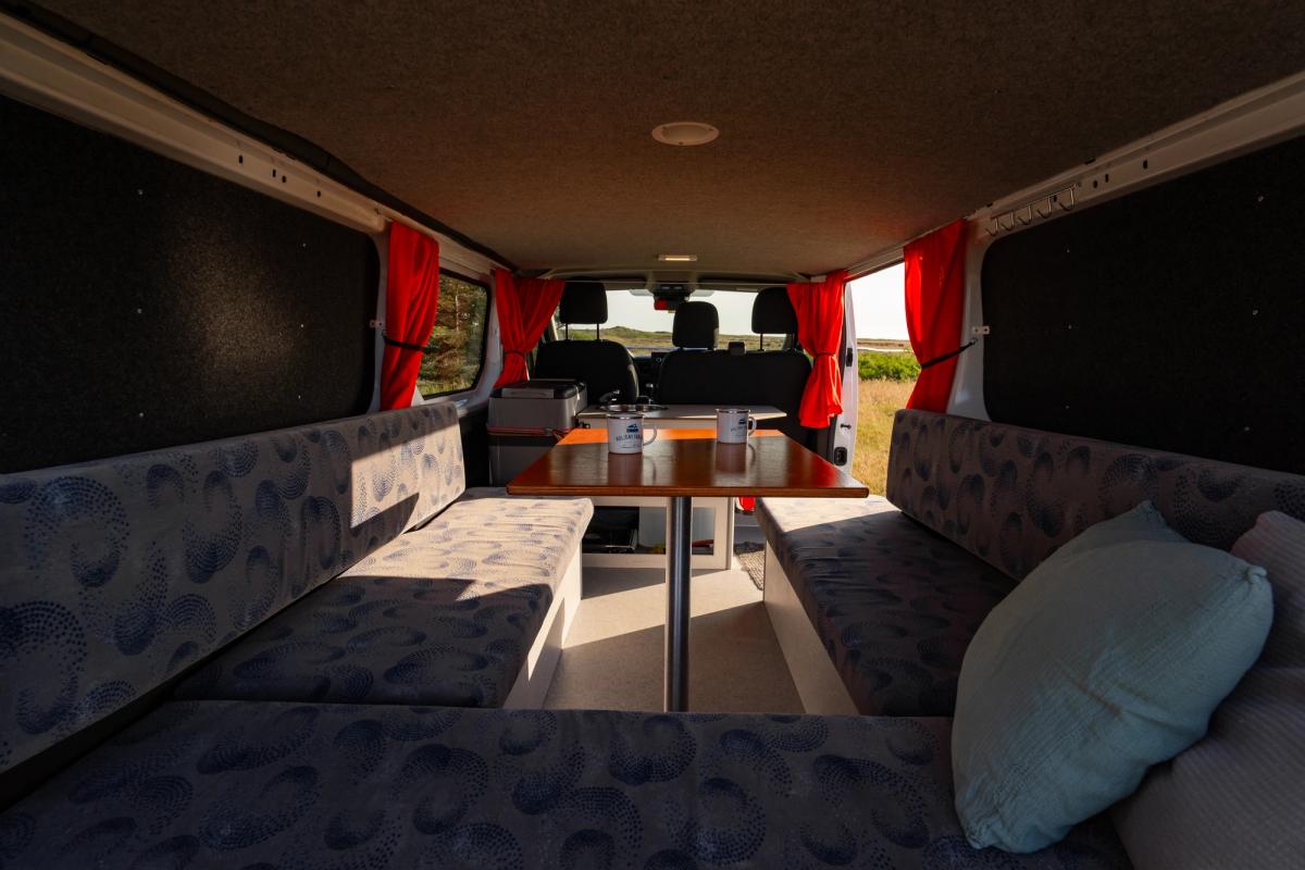 Seating area with 2 mugs on the table, viewed from the rear bench toward the cab