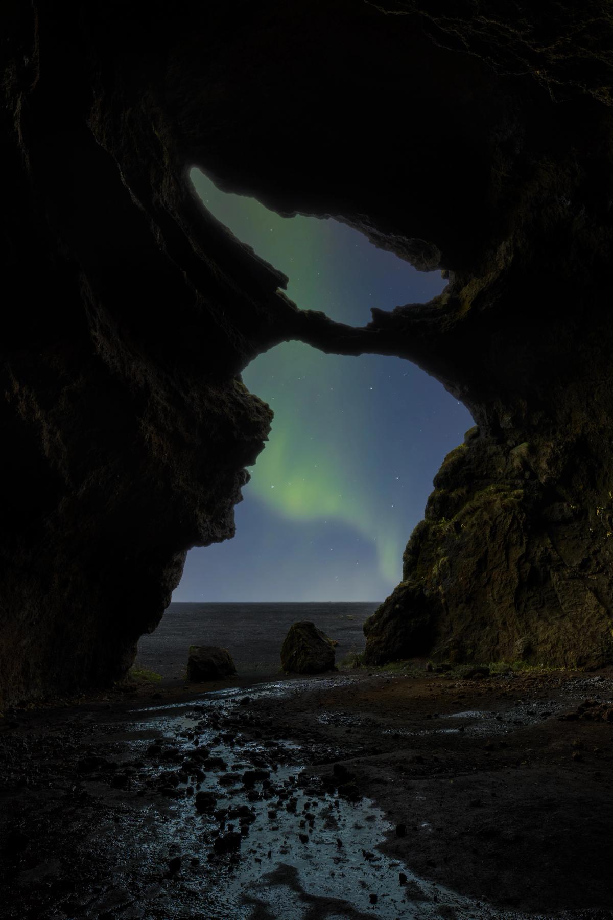 Green Northern Lights visible through dark cave openings above a dark sea.