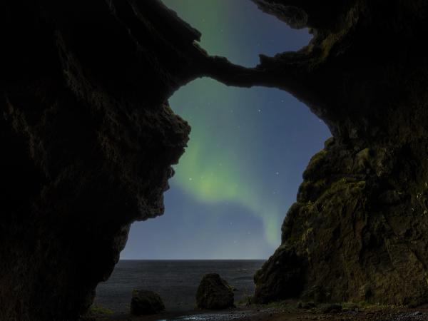 Green Northern Lights visible through dark cave openings above a dark sea.