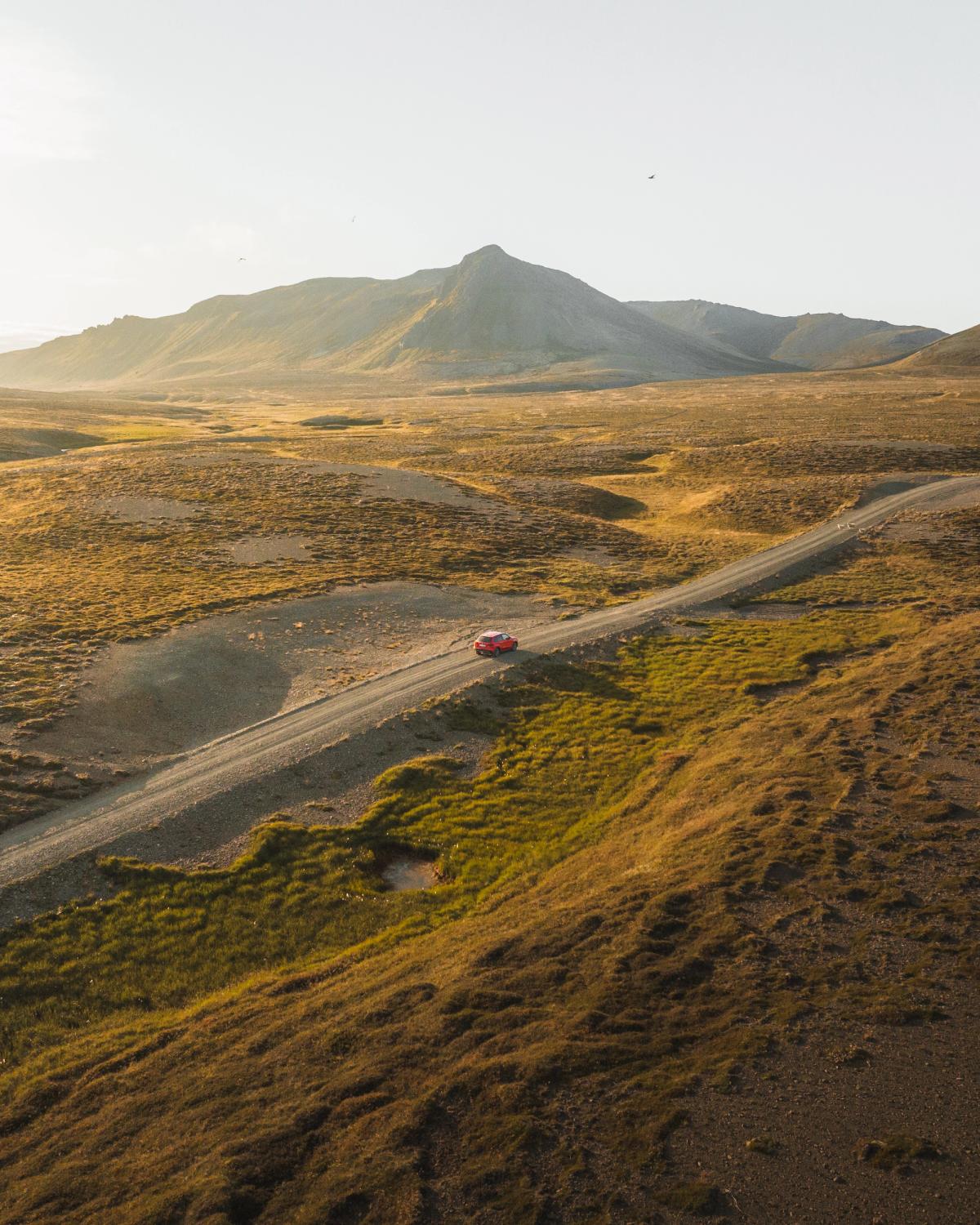 an aerial view of a red car driving down a dirt road .