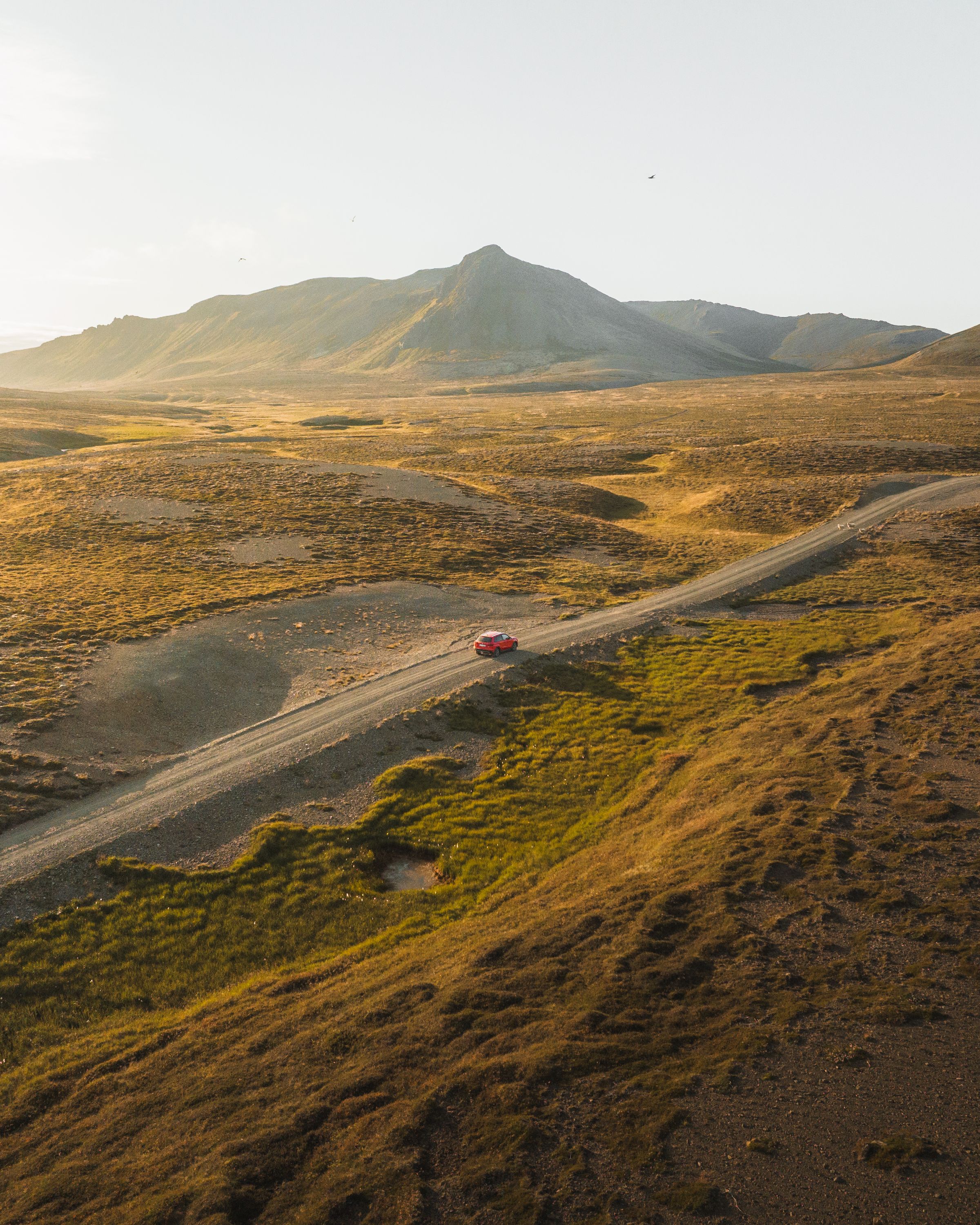 Petite Suzuki Vitara rouge sur une route de gravier traversant un paysage montagneux dégagé