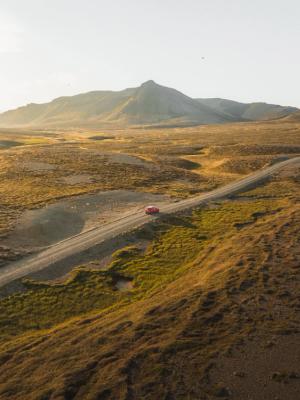an aerial view of a red car driving down a dirt road .