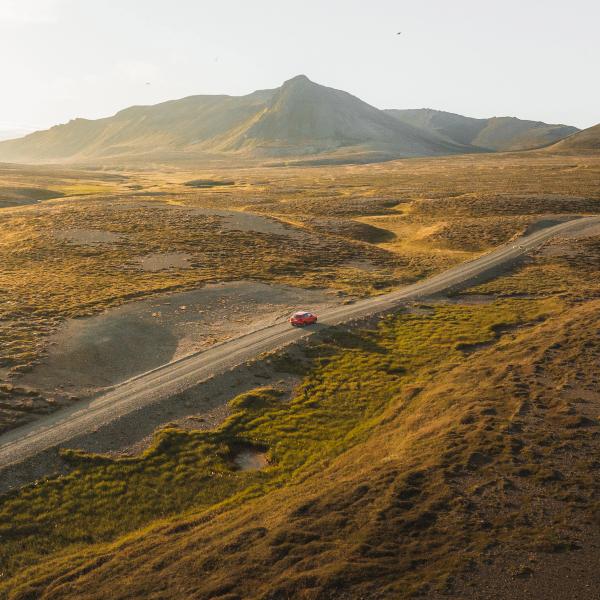 una vista aérea de un coche rojo conduciendo por un camino de tierra.