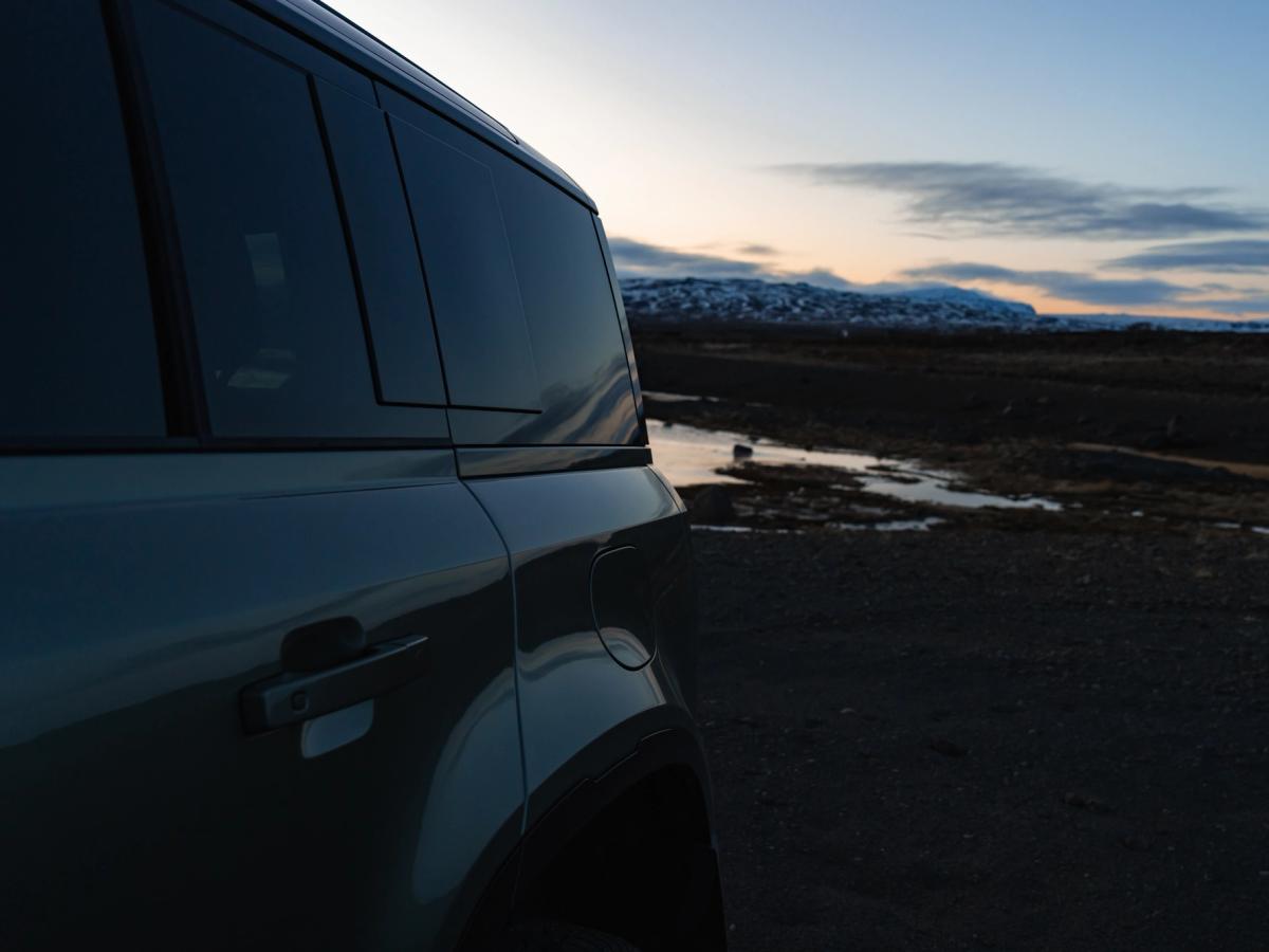 Vista lateral del Land Rover Defender al anochecer Vista lateral de la puerta y la ventanilla de un Land Rover Defender de alquiler al atardecer, con montañas al fondo, disponible en Go Car Rental Iceland