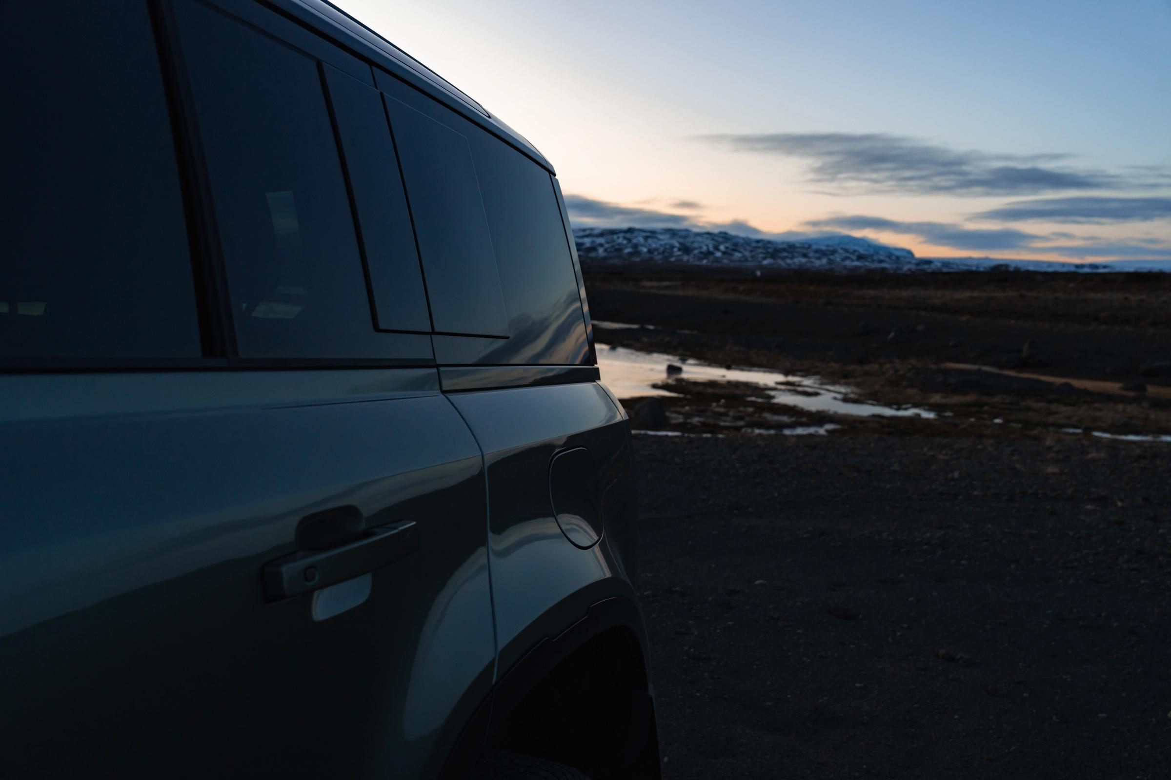 Vista lateral del Land Rover Defender al anochecer Vista lateral de la puerta y la ventanilla de un Land Rover Defender de alquiler al atardecer, con montañas al fondo, disponible en Go Car Rental Iceland