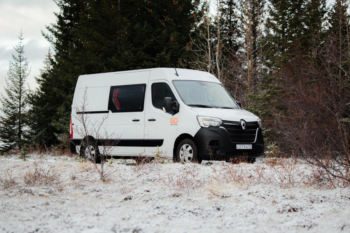 Ein geräumiger, preisgünstiger Camper für 5 Personen mit 5 Sitzplätzen, geparkt neben Nadelbäumen, Camper mieten in Island