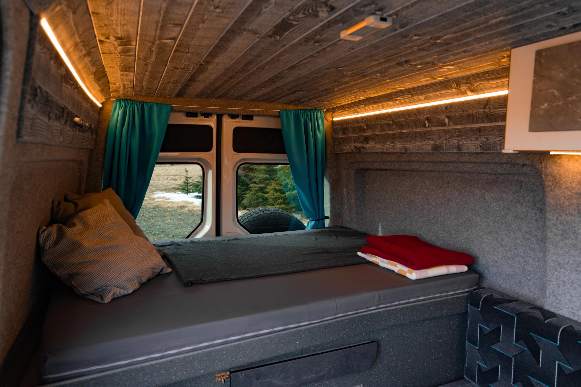 Plataforma de cama con ropa de cama roja doblada y una almohada, con las cortinas de la ventana trasera recogidasPlataforma de cama con ropa de cama roja doblada y una almohada, con las cortinas de la ventana trasera recogidas
