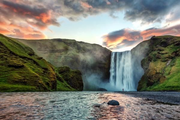 a powerful waterfall surrounded by green cliffs at sunset
