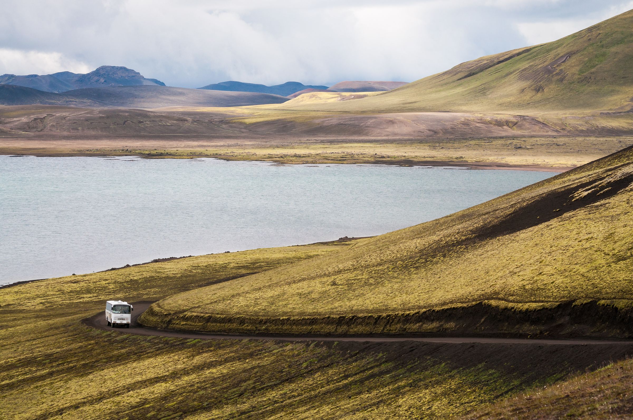 une camionnette blanche roule sur un chemin de terre à côté d'un lac .