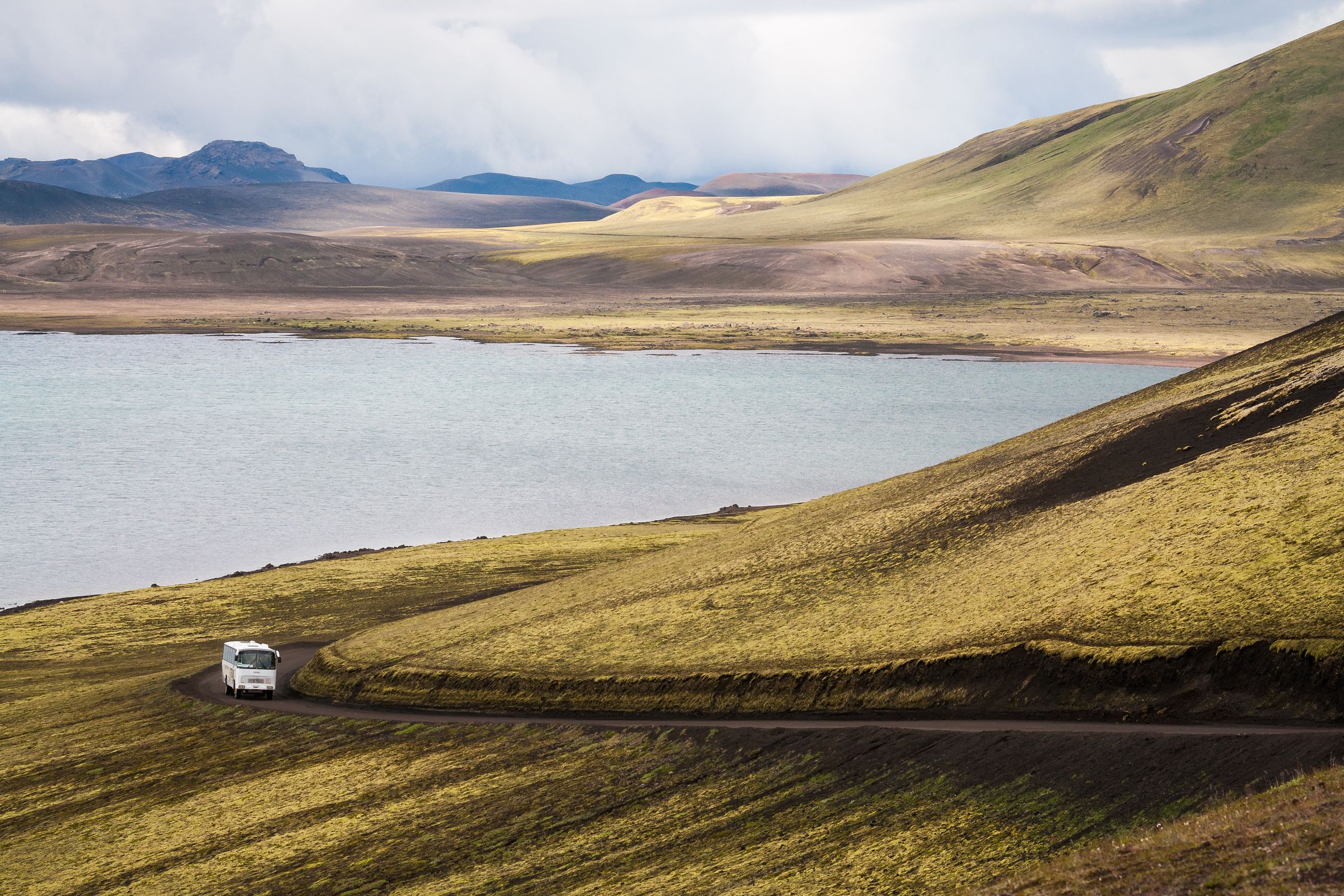 une camionnette blanche roule sur un chemin de terre à côté d'un lac .