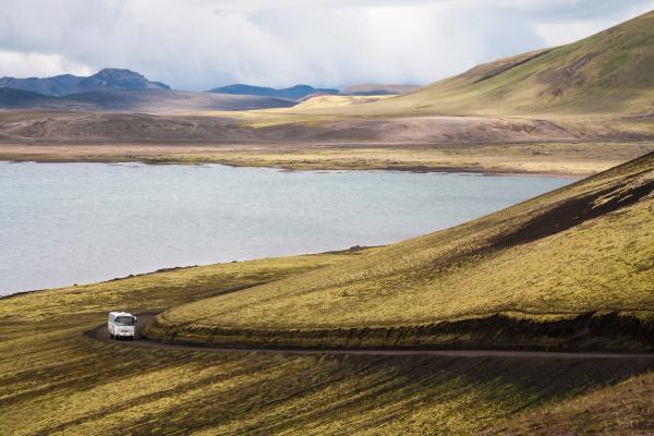 une camionnette blanche roule sur un chemin de terre à côté d'un lac .