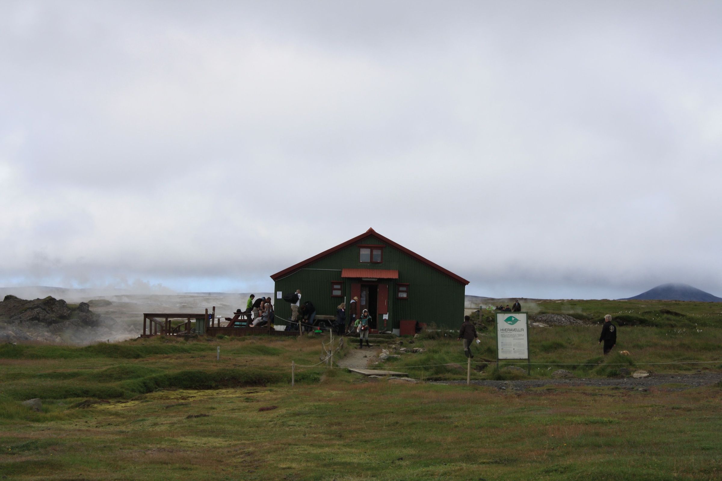 a green house with a red roof is sitting on top of a grassy hill .