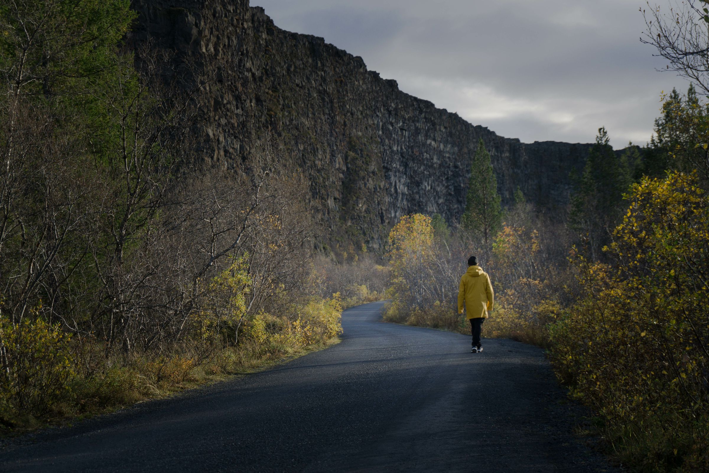 Person walking in the middle of a road surrounded by cliffs